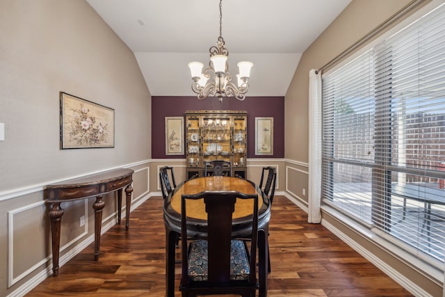 dining space with wainscoting, a notable chandelier, vaulted ceiling, and wood finished floors