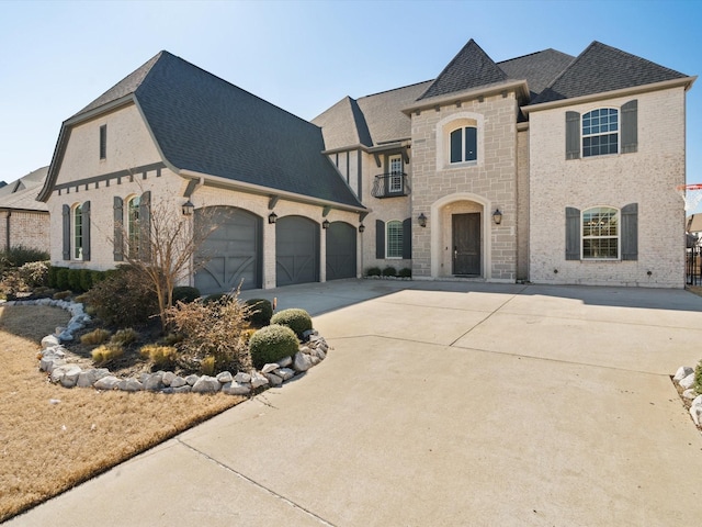 french provincial home with an attached garage, brick siding, driveway, stone siding, and roof with shingles