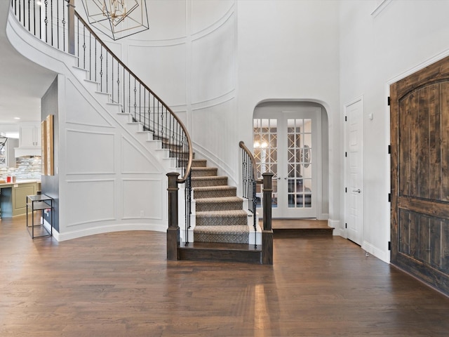 entrance foyer featuring arched walkways, a notable chandelier, a decorative wall, wood finished floors, and stairs