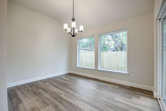 unfurnished room with lofted ceiling, a notable chandelier, wood finished floors, and baseboards