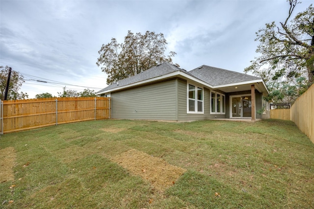 back of house featuring a yard, roof with shingles, and a fenced backyard