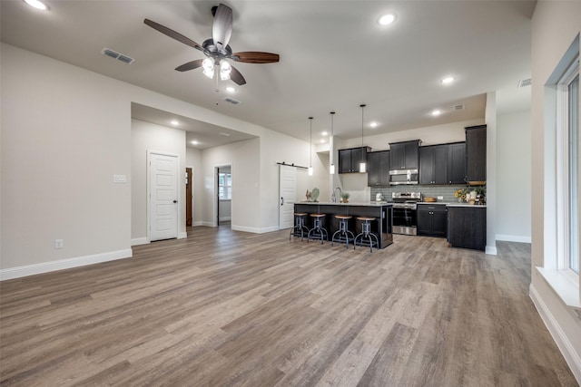 kitchen featuring a barn door, visible vents, appliances with stainless steel finishes, dark cabinetry, and a kitchen bar