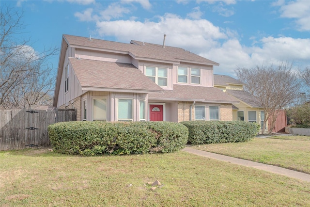 view of front facade with roof with shingles, brick siding, a front lawn, and fence