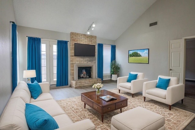 living room with high vaulted ceiling, a fireplace, visible vents, and wood finished floors