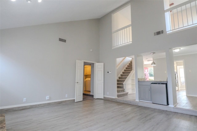 unfurnished living room featuring light wood-style flooring, visible vents, stairway, and baseboards