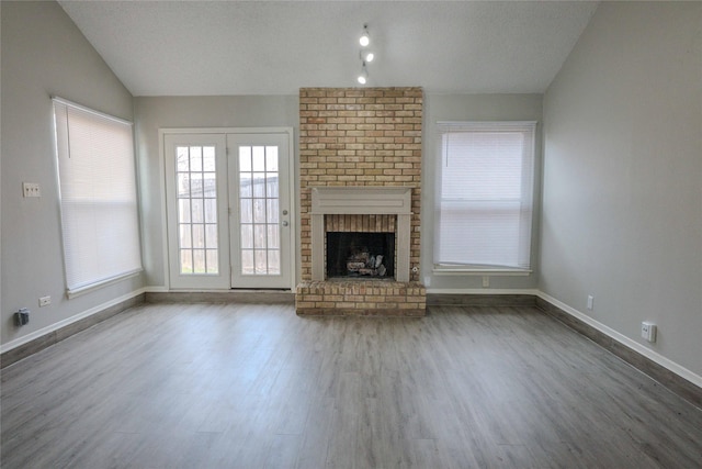 unfurnished living room with lofted ceiling, a textured ceiling, wood finished floors, baseboards, and a brick fireplace