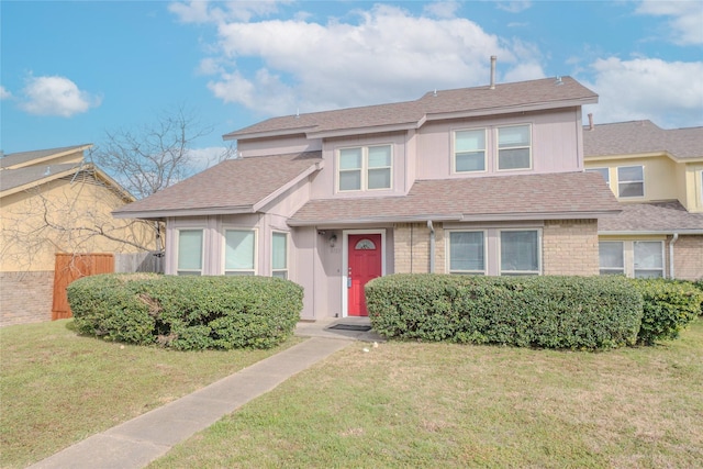 view of front of house featuring brick siding, fence, a front lawn, and roof with shingles