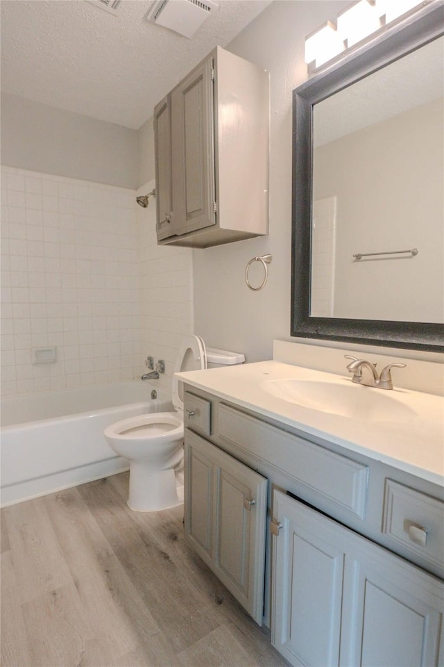 full bath featuring toilet, wood finished floors, vanity, visible vents, and tub / shower combination