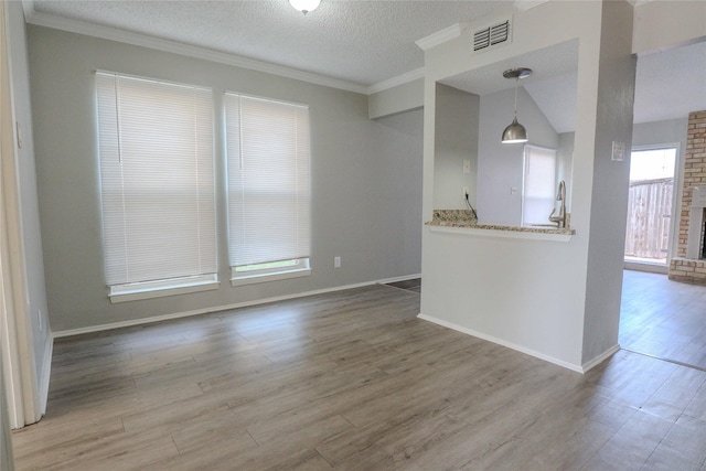 unfurnished room with a textured ceiling, wood finished floors, visible vents, ornamental molding, and a brick fireplace