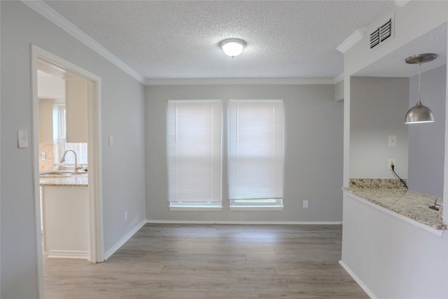 unfurnished dining area with a textured ceiling, a sink, visible vents, light wood-type flooring, and crown molding