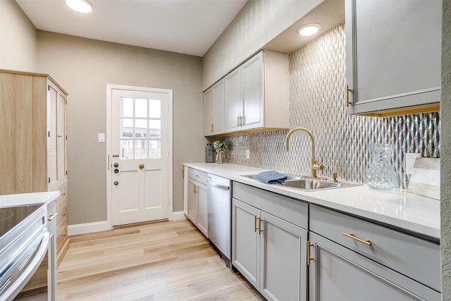 kitchen featuring light wood finished floors, tasteful backsplash, dishwasher, gray cabinets, and a sink