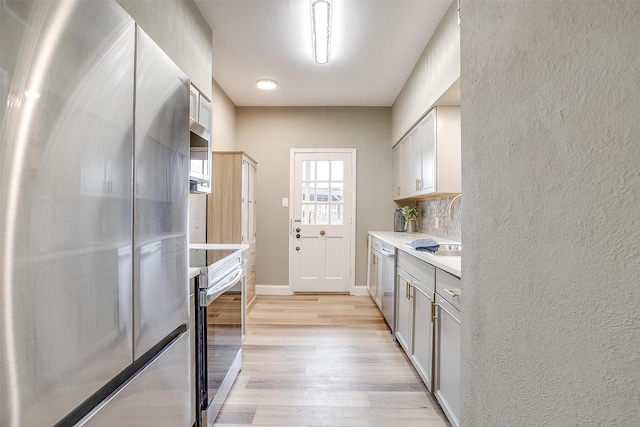 kitchen with a textured wall, light countertops, appliances with stainless steel finishes, light wood finished floors, and tasteful backsplash