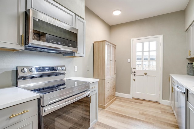 kitchen featuring stainless steel appliances, gray cabinets, light countertops, light wood-type flooring, and baseboards