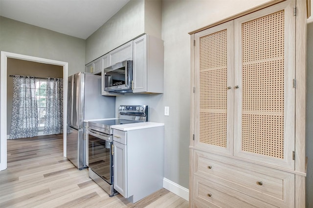 kitchen featuring light wood-style floors, baseboards, stainless steel appliances, and light countertops