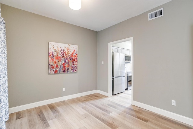 spare room featuring light wood-style flooring, visible vents, and baseboards