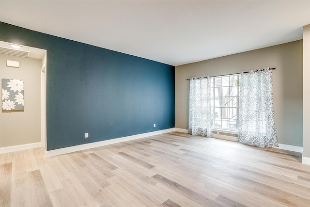 spare room with wood finished floors, visible vents, and baseboards