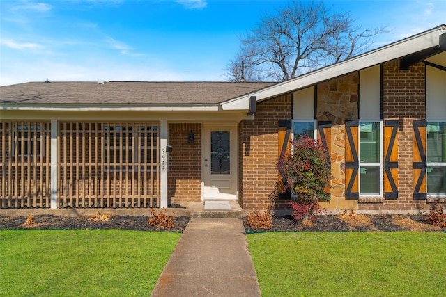 view of front of property featuring a shingled roof, a front lawn, and brick siding