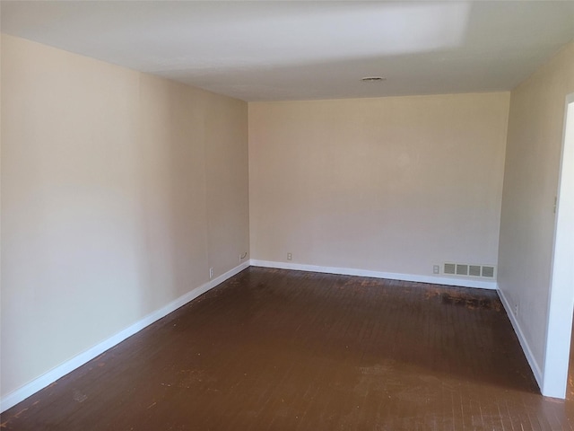 spare room featuring dark wood finished floors, visible vents, and baseboards