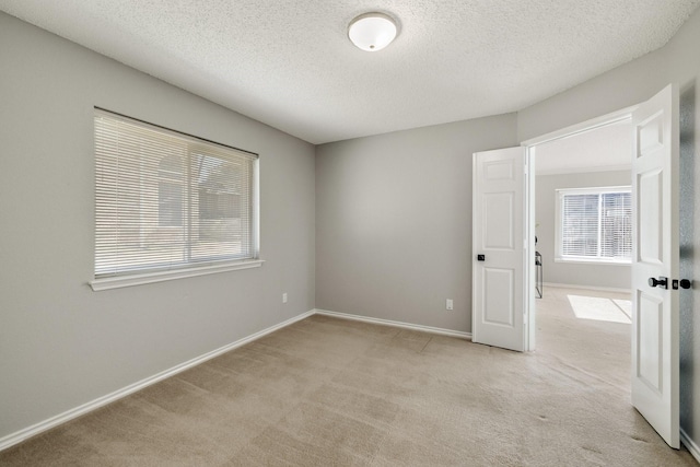 empty room with light colored carpet, a textured ceiling, and baseboards