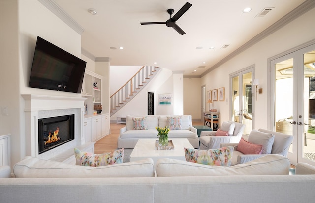living area featuring ornamental molding, a high end fireplace, french doors, and light wood finished floors