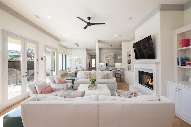 living area featuring built in shelves, light wood-style flooring, french doors, a glass covered fireplace, and crown molding