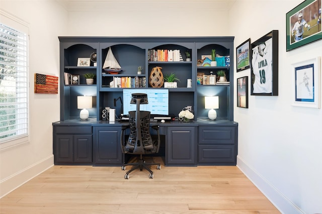 office space with built in desk, crown molding, and light wood-style flooring