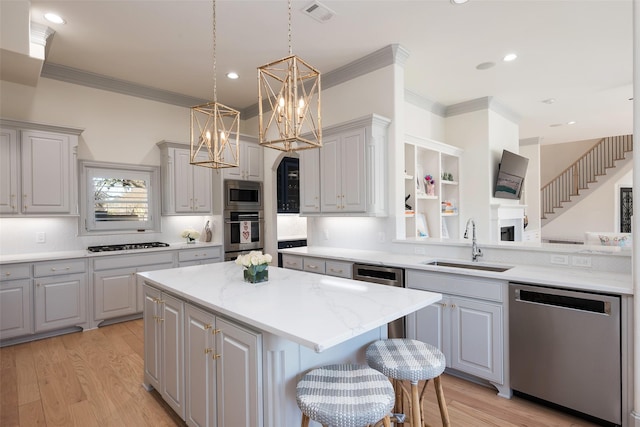 kitchen featuring light wood-style flooring, a sink, appliances with stainless steel finishes, gray cabinets, and a center island