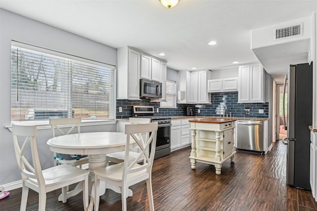 kitchen with appliances with stainless steel finishes, visible vents, wood counters, and decorative backsplash