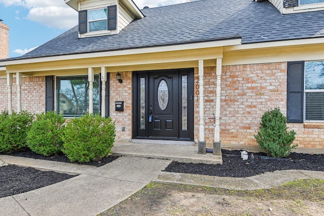 doorway to property with roof with shingles and brick siding