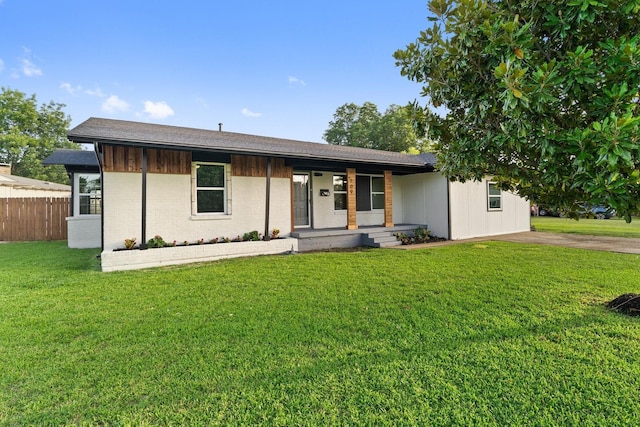 view of front of home with a front yard, covered porch, brick siding, and fence