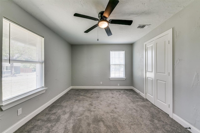 empty room with a textured ceiling, ceiling fan, visible vents, baseboards, and carpet