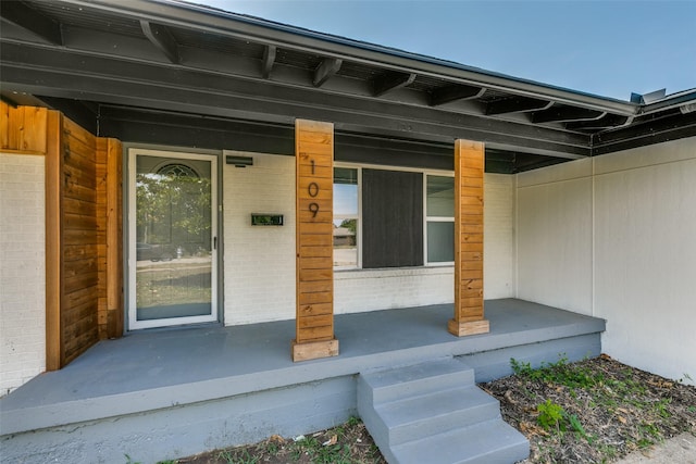 entrance to property with covered porch and brick siding