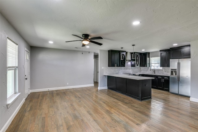 kitchen with dark cabinetry, light countertops, backsplash, wood finished floors, and stainless steel fridge