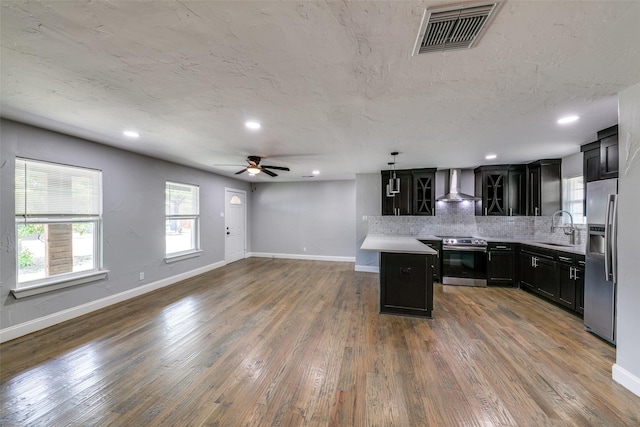 kitchen featuring visible vents, open floor plan, stainless steel appliances, dark cabinetry, and wall chimney range hood
