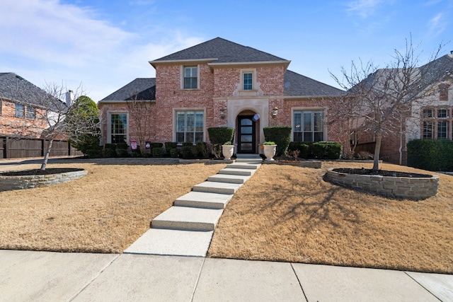 view of front facade with a shingled roof, a front yard, fence, and brick siding