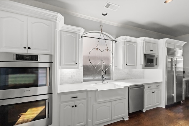 kitchen featuring white cabinets, visible vents, a sink, and built in appliances