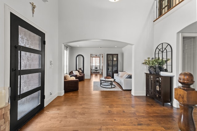 entryway featuring arched walkways, a towering ceiling, baseboards, and wood finished floors