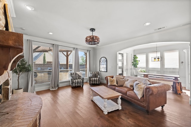 living room featuring a large fireplace, visible vents, arched walkways, wood finished floors, and a notable chandelier