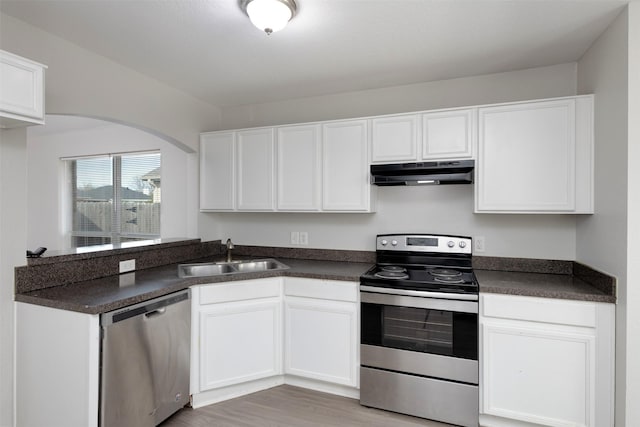 kitchen with dark countertops, stainless steel appliances, under cabinet range hood, white cabinetry, and a sink