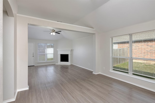 unfurnished living room featuring lofted ceiling, a fireplace with raised hearth, baseboards, and wood finished floors