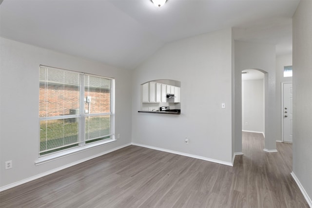 empty room featuring arched walkways, lofted ceiling, baseboards, and wood finished floors