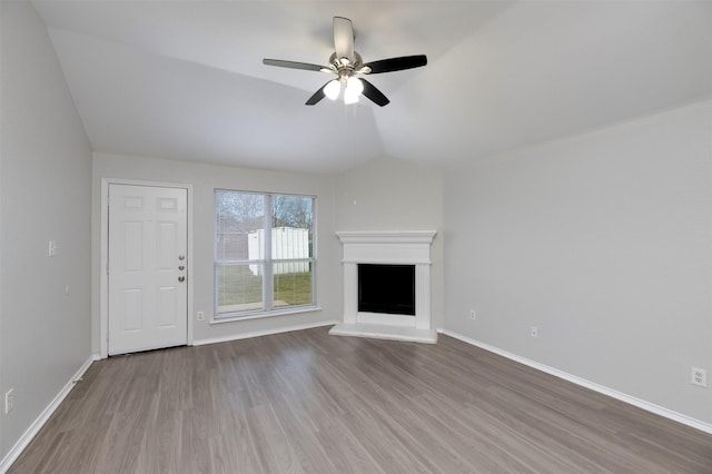 unfurnished living room with vaulted ceiling, a fireplace with raised hearth, wood finished floors, and baseboards