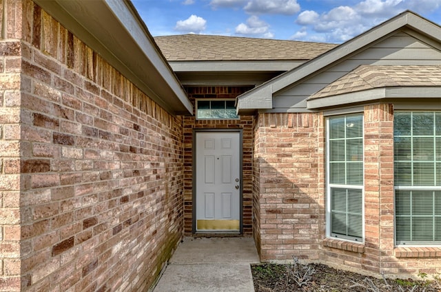 view of exterior entry featuring a shingled roof and brick siding