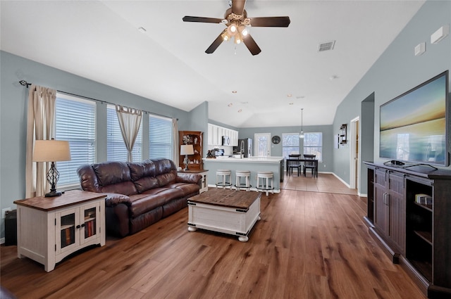 living area with vaulted ceiling, wood finished floors, visible vents, and baseboards