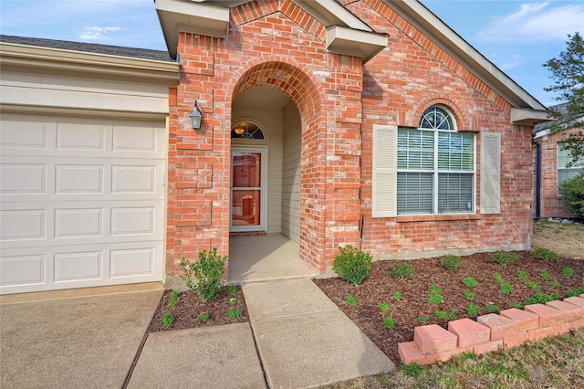 view of exterior entry featuring a garage and brick siding