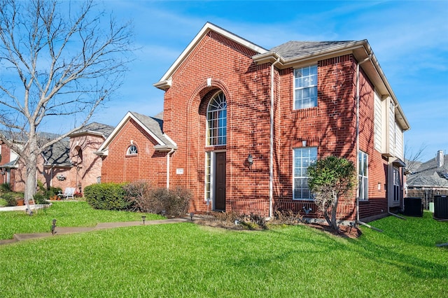 view of front of house featuring cooling unit, brick siding, and a front lawn