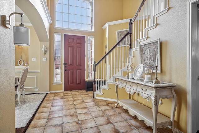 tiled foyer entrance with a towering ceiling, stairs, and baseboards