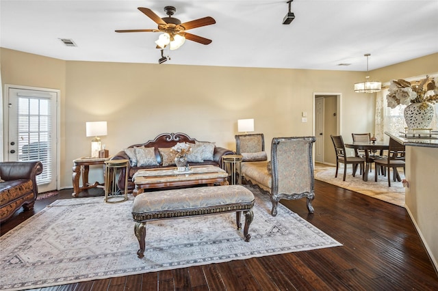 living area with ceiling fan with notable chandelier, hardwood / wood-style floors, visible vents, and baseboards