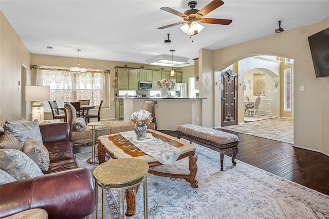 living area featuring visible vents, arched walkways, a ceiling fan, baseboards, and wood finished floors