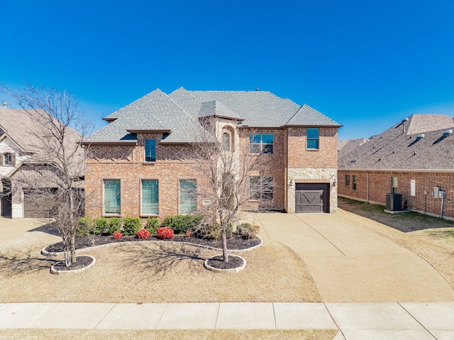 view of front facade with central AC unit, an attached garage, brick siding, a shingled roof, and driveway